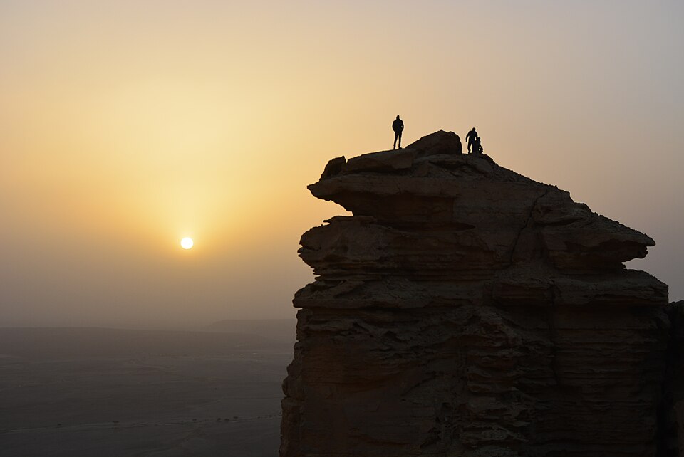 Dos personas sobre la punta de un acantilado al atardecer en el Borde del Mundo