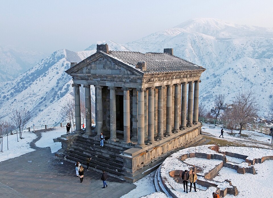 El templo de Garni con columnas de piedra rodeado de montañas nevadas