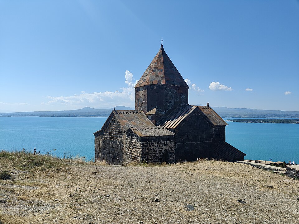 La iglesia de piedra oscura de Sevanavank frente al agua azul del lago Seván