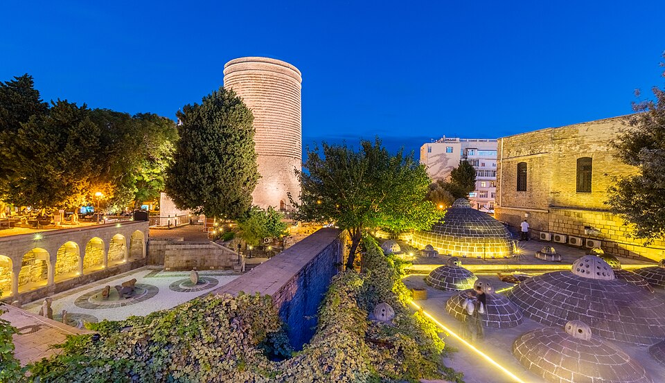 La Torre de la Doncella iluminada junto a jardines y ruinas en la Ciudad Vieja de Bakú