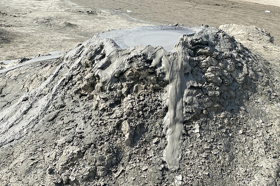 Un pequeño volcán de lodo gris con una colada de barro fresco