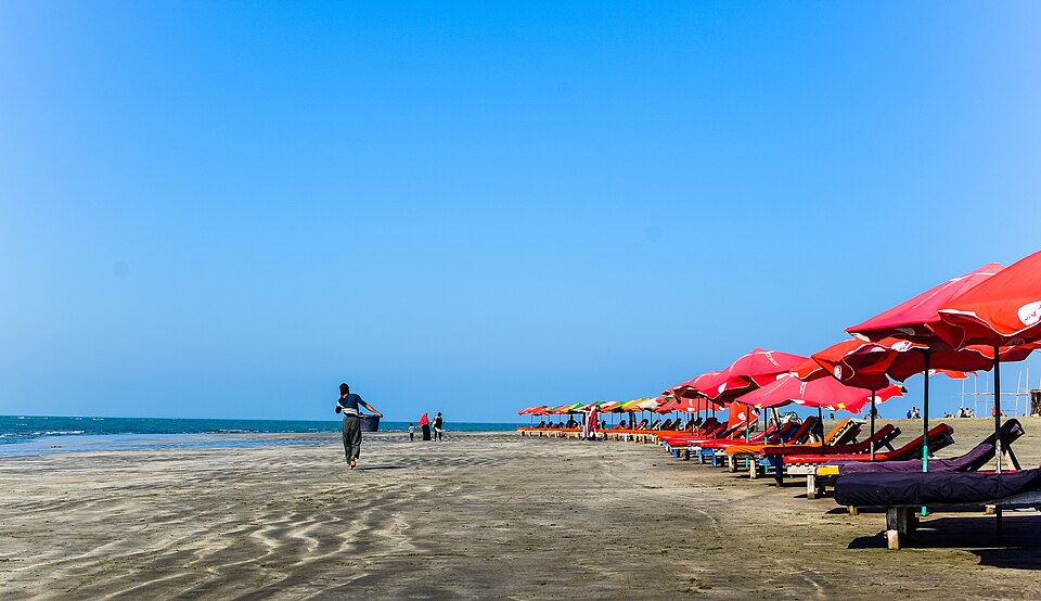 La playa de Cox's Bazar con sombrillas rojas bajo un cielo azul