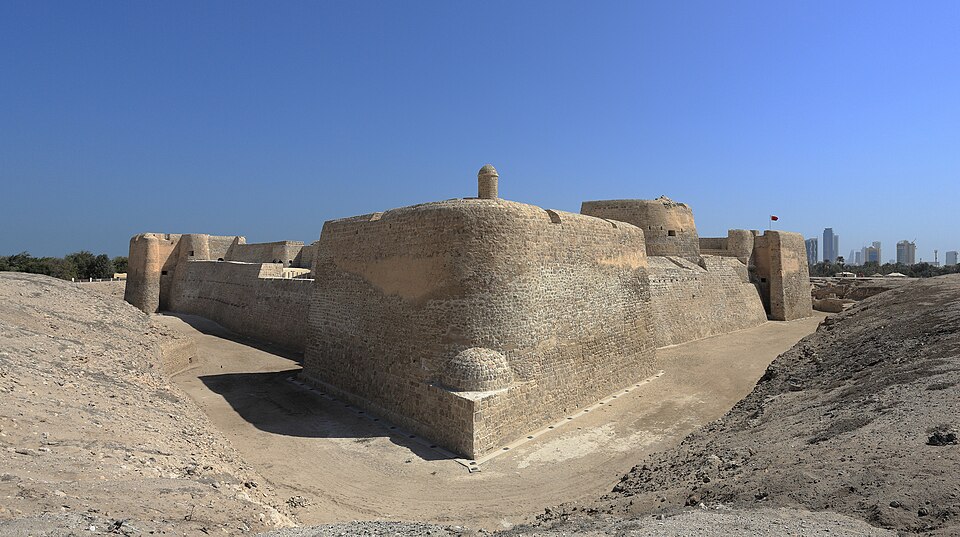 Los muros de piedra del fuerte de Qal'at al-Bahrain con rascacielos al fondo