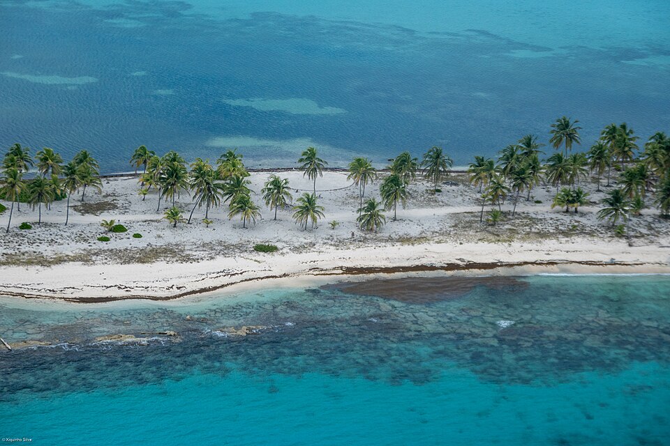 Cayo con palmeras y arena blanca junto a la barrera de coral en agua turquesa