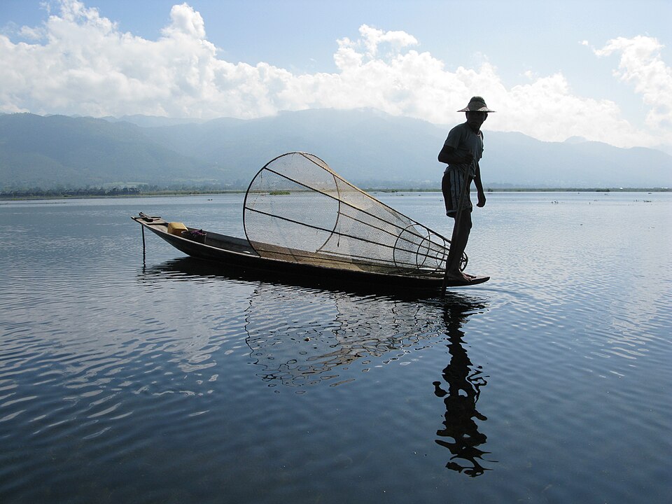 Un pescador de pie en su lancha sosteniendo una red cónica en el lago Inle