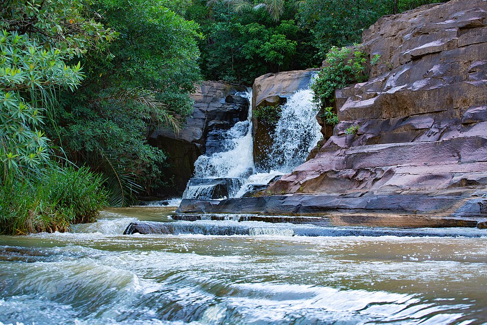 Cascada que cae entre rocas rosadas y vegetación en Karfiguéla
