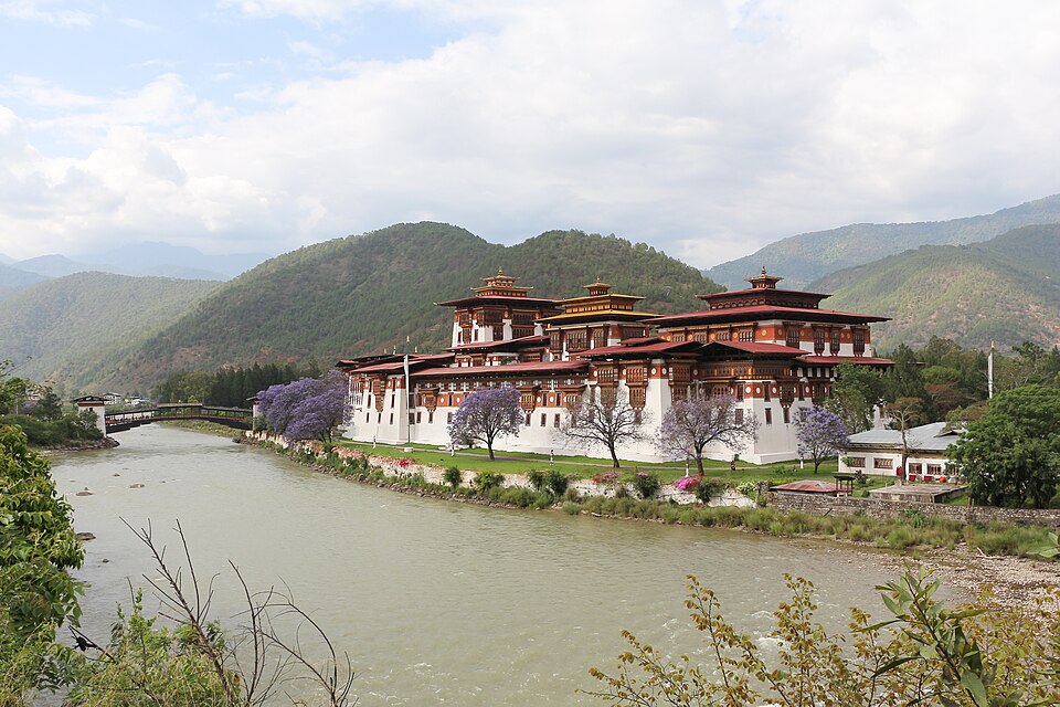 El dzong de Punakha junto al río con jacarandas en flor y montañas detrás