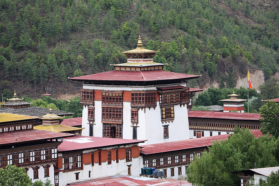 El dzong de Tashichho con su torre blanca y techos dorados al pie de un bosque