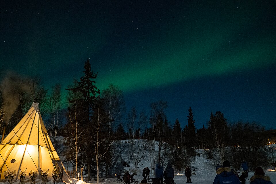 Aurora boreal verde sobre un bosque nevado y un tipi iluminado cerca de Yellowknife