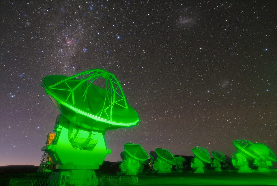 Antenas del observatorio ALMA iluminadas de verde bajo un cielo lleno de estrellas