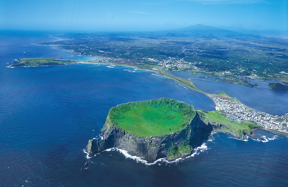 El cráter verde de Seongsan Ilchulbong rodeado de mar azul, visto desde el aire