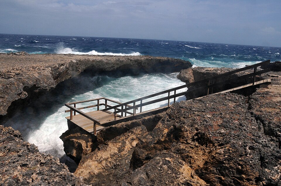 Olas que rompen dentro de una ensenada de roca en Shete Boka, con un mirador de madera