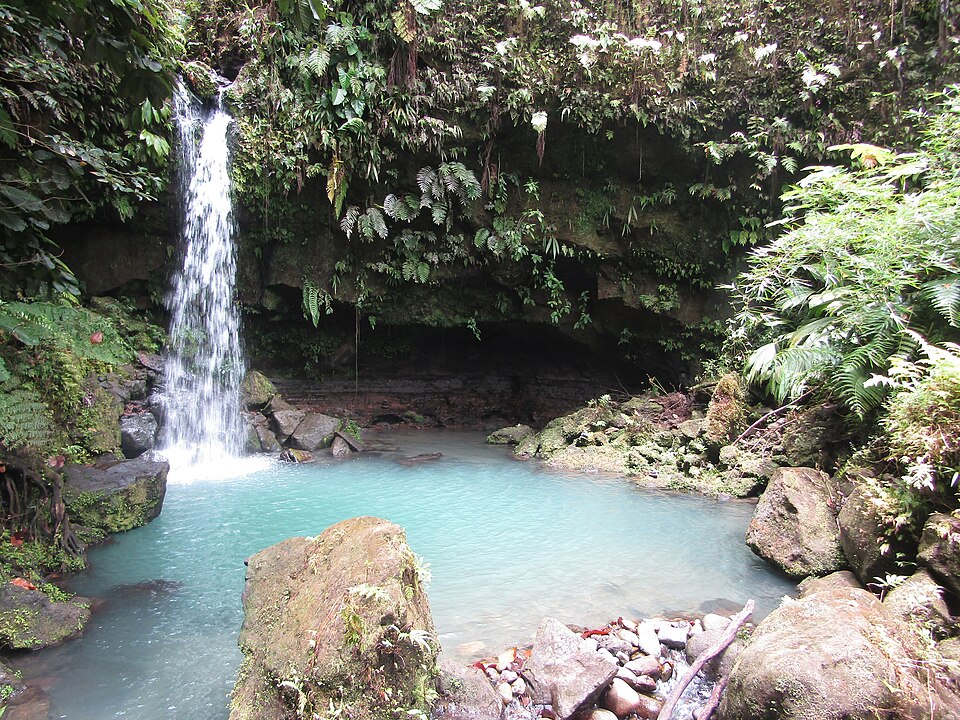 Una cascada que cae en una poza de agua turquesa rodeada de selva en Emerald Pool