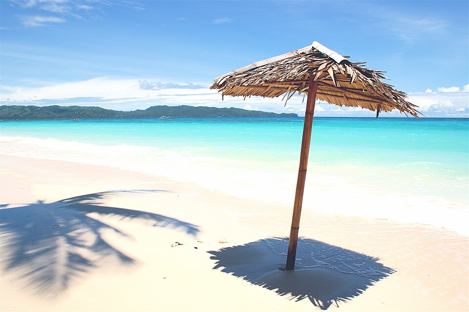Una sombrilla de palma en la arena blanca de Boracay frente al mar turquesa