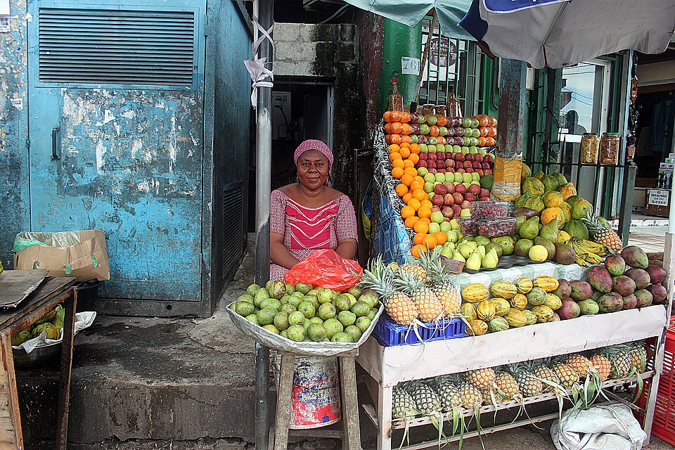 Vendedora en un puesto lleno de piñas, mangos y otras frutas tropicales en Libreville