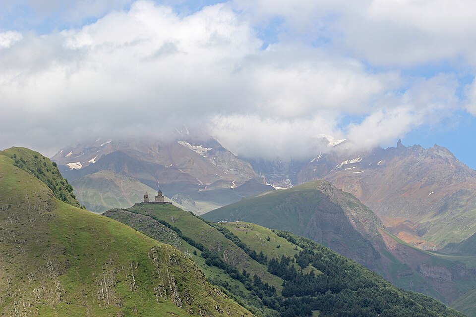 La iglesia de Gergeti en lo alto de una colina verde entre montañas
