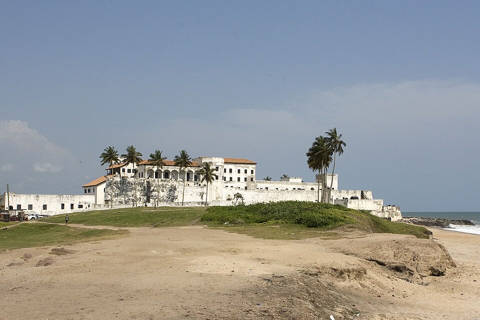 Castillo blanco de Elmina junto al mar y a la playa con palmeras