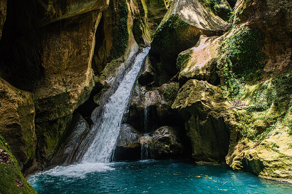 Poza de agua azul turquesa con una cascada entre rocas en Bassin Bleu