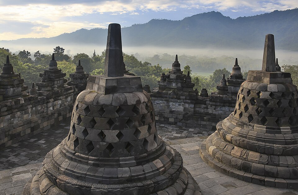 Estupas de piedra caladas en lo alto de Borobudur con montañas y niebla