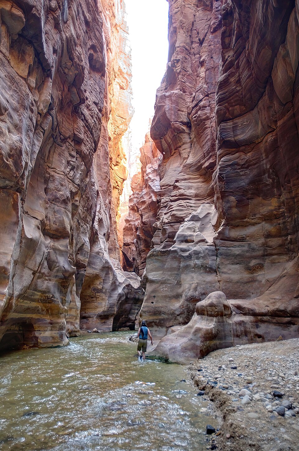Una persona caminando por el río entre las altas paredes rojas del cañón de Wadi Mujib