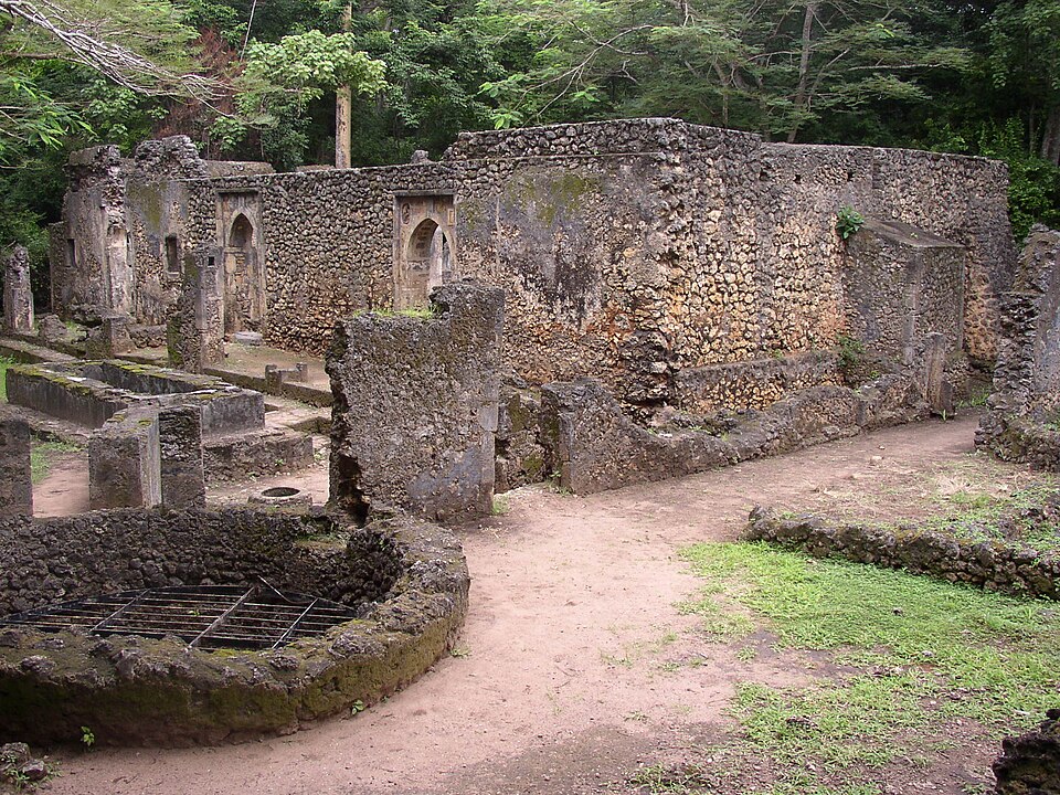 Ruinas de la Gran Mezquita de Gedi, con muros y arcos de piedra de coral entre árboles