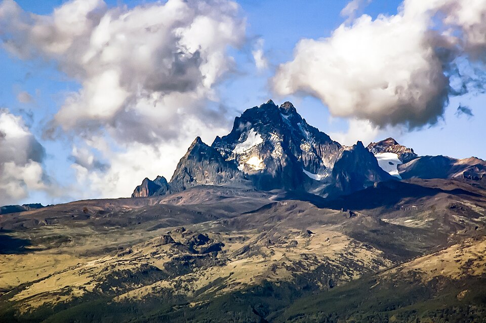Los picos rocosos y nevados del monte Kenia entre nubes, sobre laderas doradas