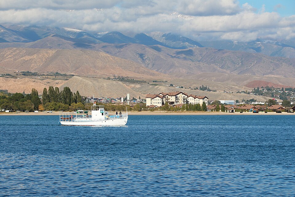 Un barco en el agua azul del lago Issyk-Kul con montañas detrás