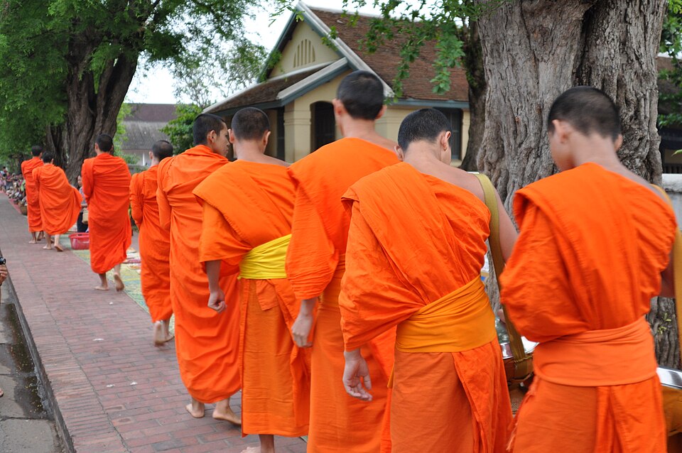 Monjes con túnicas naranjas caminando en fila por una calle