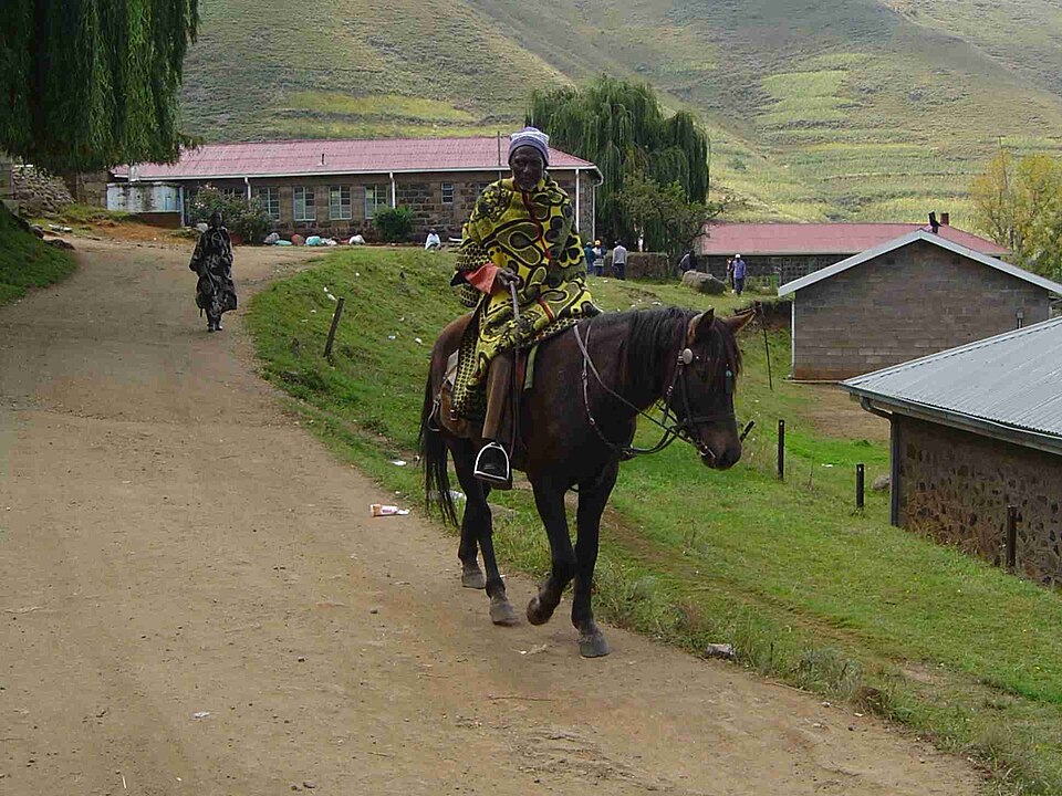 Jinete basoto envuelto en una manta de colores sobre un caballo en un camino de aldea