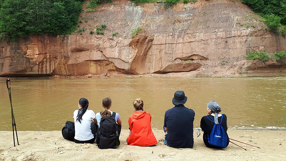 Excursionistas frente a un acantilado de arenisca roja junto al río Gauja