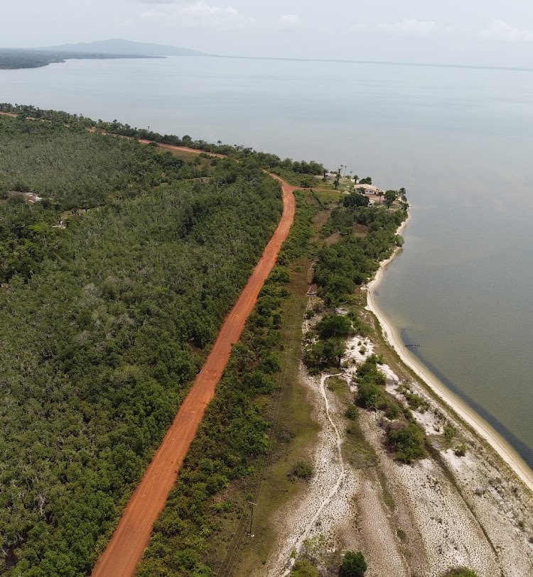 Vista aérea de una franja de bosque con un camino rojo entre el lago Piso y el mar