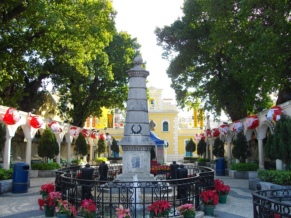 La plaza de Coloane con un monumento y la capilla amarilla al fondo