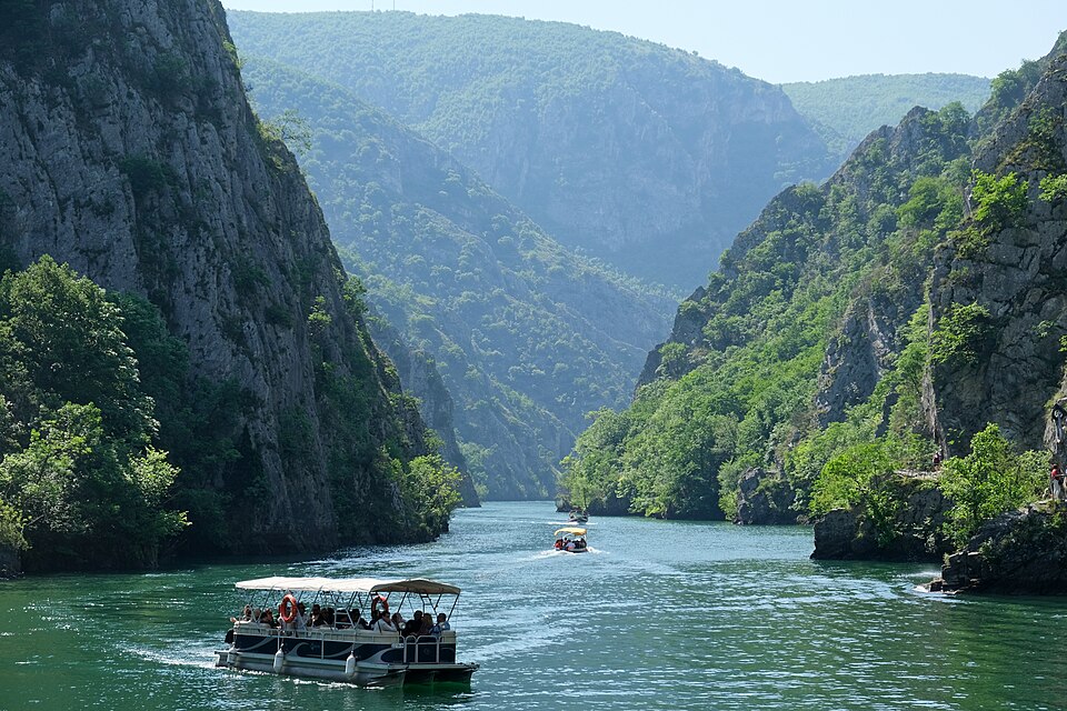 Una lancha navegando por el cañón de Matka entre montañas verdes