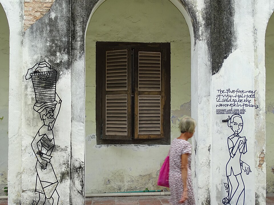 Una mujer pasa frente a dibujos en la pared de una casa antigua en George Town