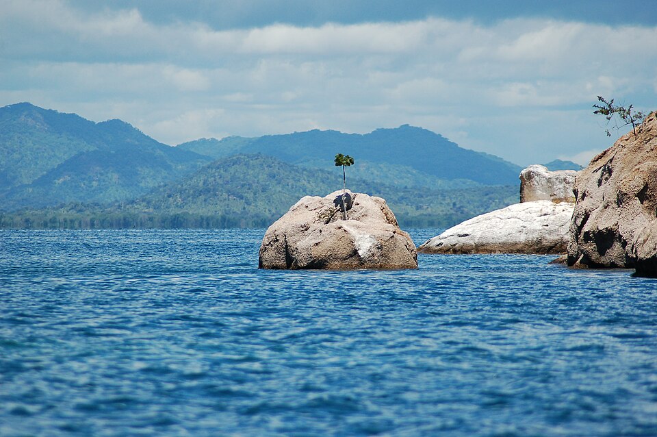 Rocas grandes en el agua azul del lago Malaui frente a cerros verdes en Cabo Maclear