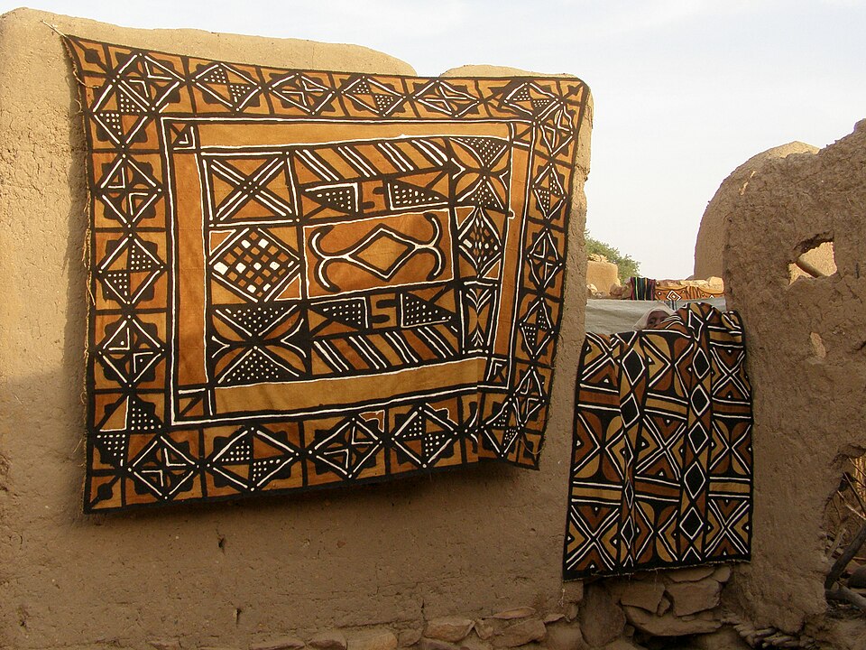 Telas de bogolan con dibujos geométricos colgadas sobre un muro de barro en Sangha