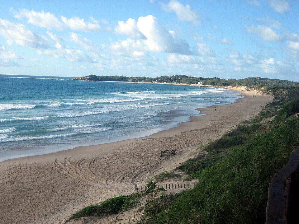 Playa larga de Tofo con olas y dunas cubiertas de vegetación