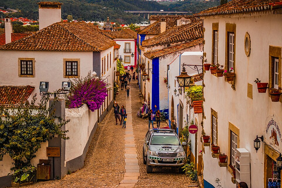 Una calle empedrada de Óbidos con casas blancas y flores