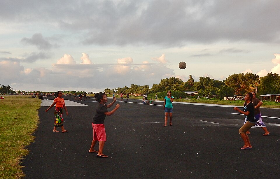 Jóvenes jugando voleibol en la pista del aeropuerto de Funafuti al atardecer